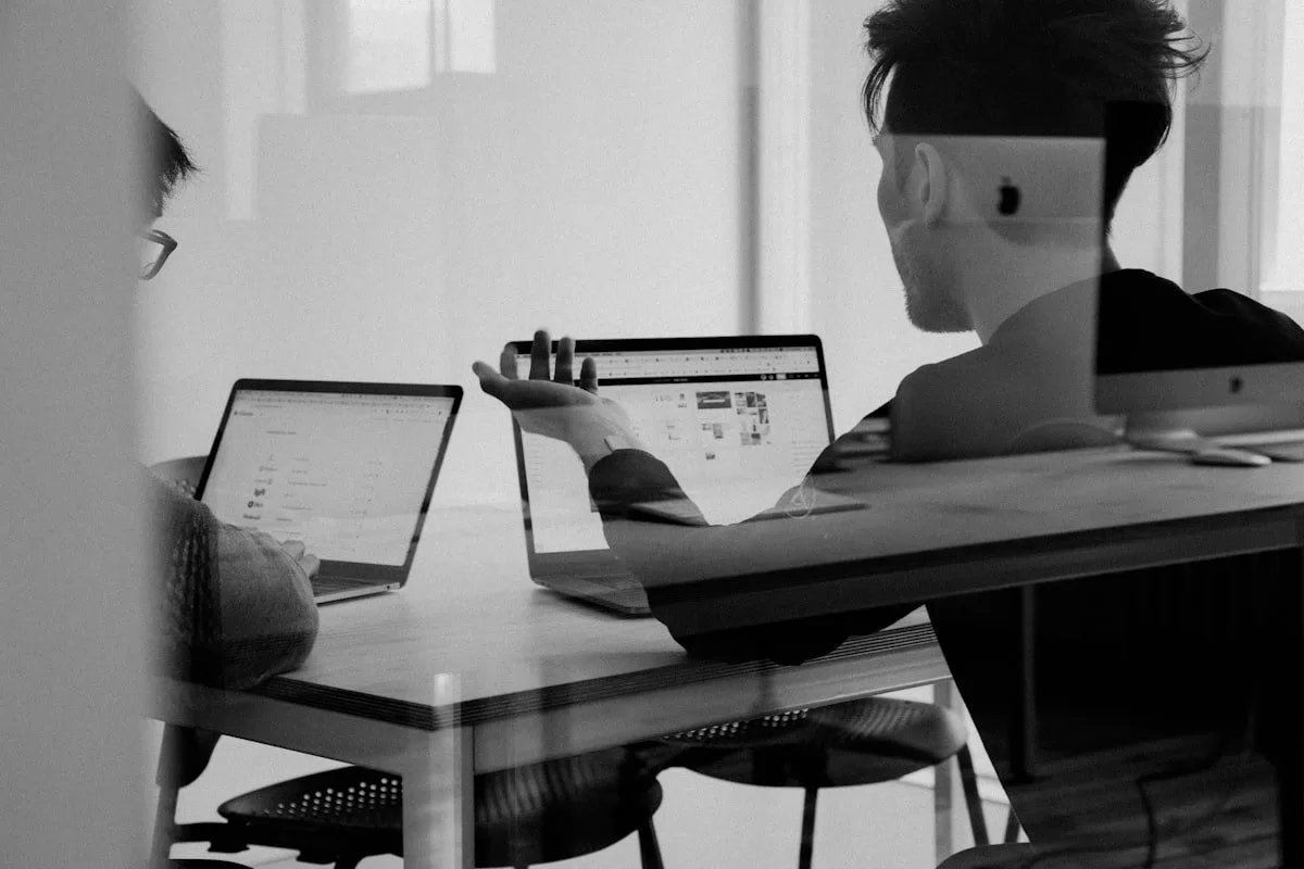 Twee mensen achter laptops aan een bureau, in zwart-wit